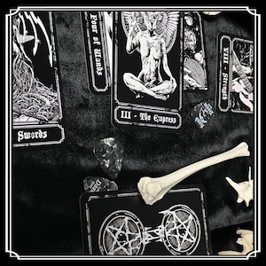 Peut inclure: Cartes de tarot noir et blanc dispos&eacute;es sur une surface noire. Les cartes montrent des images d'une femme ail&eacute;e, d'une &eacute;p&eacute;e et d'un os. Les cartes sont &eacute;tiquet&eacute;es avec des chiffres romains et les noms des cartes. Il y a aussi des m&eacute;diators avec le mot "Doom" dessus.