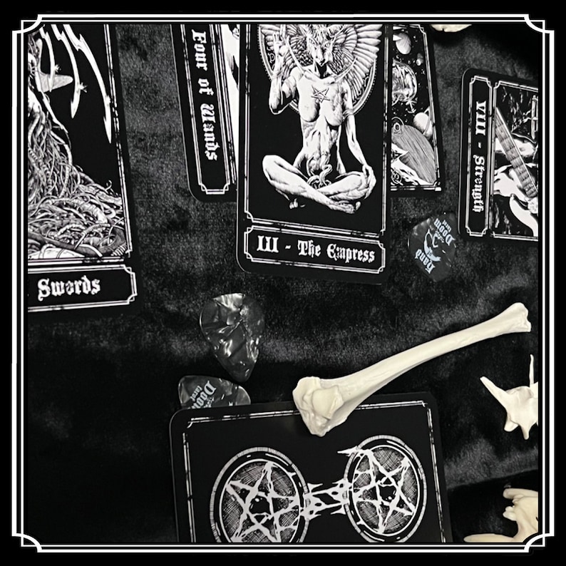 Peut inclure: Cartes de tarot noir et blanc dispos&eacute;es sur une surface noire. Les cartes montrent des images d'une femme ail&eacute;e, d'une &eacute;p&eacute;e et d'un os. Les cartes sont &eacute;tiquet&eacute;es avec des chiffres romains et les noms des cartes. Il y a aussi des m&eacute;diators avec le mot "Doom" dessus.