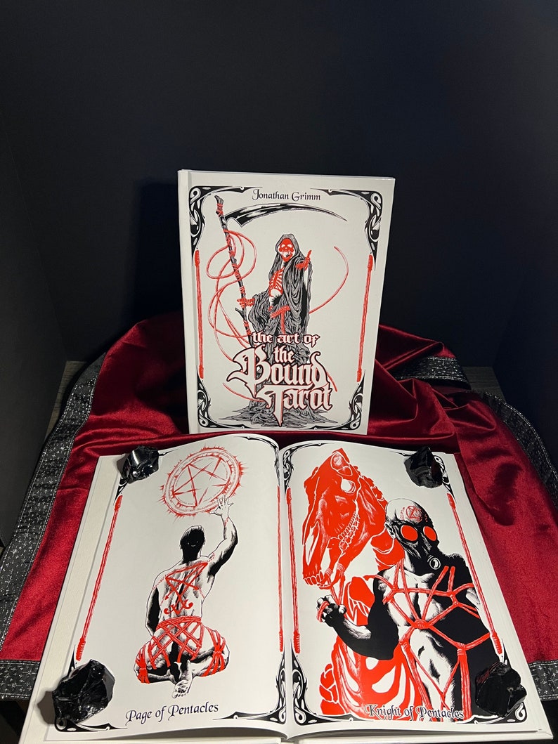 May include: A book titled "The Art of the Bound Tarot" by Jonathan Grimm. The cover features a skeletal figure in a hooded robe holding a scythe. The book is open to two pages, showing illustrations of the Page of Pentacles and the Knight of Pentacles.