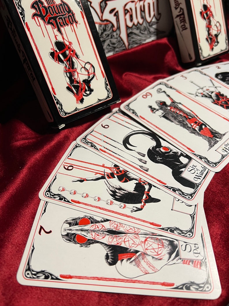 May include: A set of tarot cards with black and white illustrations and red accents. The cards feature a variety of figures and symbols, including a figure bound with ropes, a figure with a crown, and a figure with a sword. The cards are titled "The Bound Tarot".