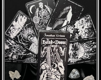 May include: A black and white tarot deck box with the title "The Hand of Doom Tarot" and the name "Jonathan Grimm". The box is surrounded by black and white tarot cards with various images.