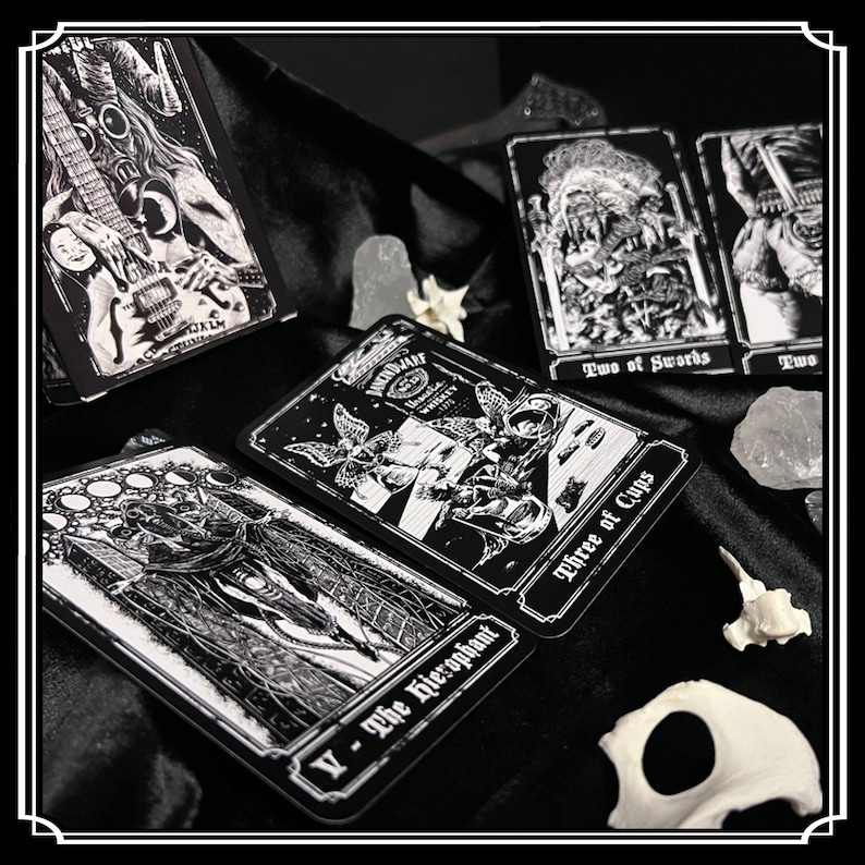 Peut inclure: Cartes de tarot noir et blanc avec des images gothiques et occultes. Les cartes pr&eacute;sentent des illustrations d'une figure squelettique avec une guitare, une figure avec une &eacute;p&eacute;e, une figure avec une coupe et une figure avec une couronne. Les cartes sont dispos&eacute;es sur une surface de velours noir.