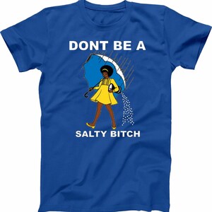 May include: Royal blue t-shirt with the text "DONT BE A SALTY BITCH". The graphic features a woman in a yellow dress under a blue umbrella, with salt pouring out. The design is printed on the front of the shirt.