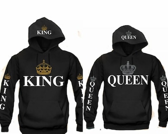 Könnte beinhalten: Zwei schwarze Kapuzenpullover mit weißem Text und goldenen oder silbernen Kronen. Einer trägt die Aufschrift "KING" mit einer goldenen Krone, der andere "QUEEN" mit einer silbernen Krone. Die Wörter "KING" und "QUEEN" stehen auch auf den Ärmeln.