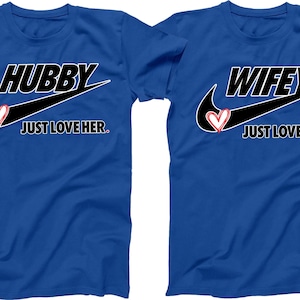 May include: Two blue t-shirts with a black swoosh and a heart design. One shirt says "Hubby Just Love Her." The other shirt says "Wifey Just Love Him."