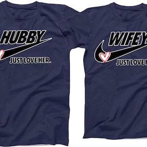 May include: Two navy blue t-shirts with a white Nike swoosh and the words "Hubby Just Love Her" and "Wifey Just Love Him" in white text. A red heart is inside the swoosh on each shirt.