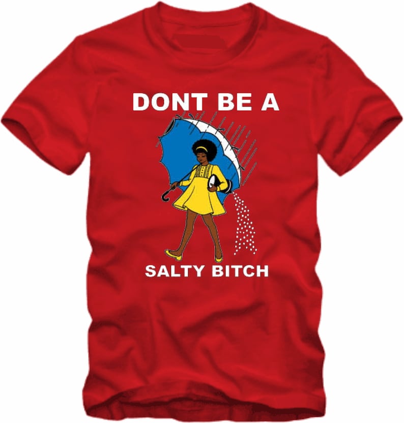May include: Red t-shirt with the text "DONT BE A SALTY BITCH". The graphic features a cartoon woman in a yellow dress and holding a blue umbrella, with salt pouring from it. The shirt is a crew neck style.