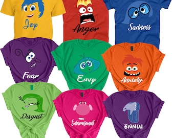 May include: Nine different colored t-shirts with cartoon characters and text. The characters are from the movie Inside Out. The colors of the shirts are yellow, red, blue, purple, green, orange, lime green, pink, and purple. The text on the shirts reads: Joy, Anger, Sadness, Fear, Envy, Anxiety, Disgust, Embarrassment, and Ennui.