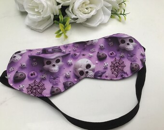 May include: Purple sleep mask with a spooky Halloween design featuring skulls, cobwebs, and other spooky elements. The mask has an adjustable black elastic strap.