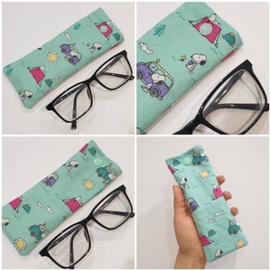 May include: Two pairs of eyeglasses with a teal blue fabric case featuring a cartoon dog and a car design. The case has a button closure.