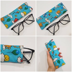 May include: A blue fabric glasses case with a colorful cartoon design featuring smiling faces, balloons, and kites. The case is shown with a pair of black framed glasses.