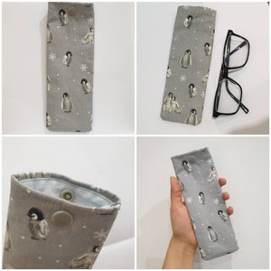 May include: A gray fabric glasses case with a penguin and snowflake pattern. The case has a button closure and is shown closed and open.