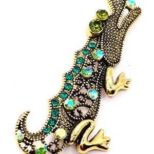 May include: A gold alligator brooch with green and iridescent rhinestones