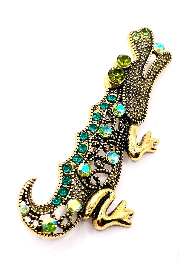 May include: A gold alligator brooch with green and iridescent rhinestones