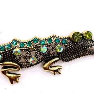 May include: A gold jeweled alligator brooch with green and iridescent rhinestones