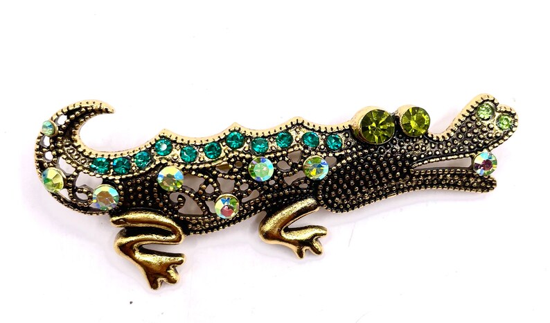 May include: A gold jeweled alligator brooch with green and iridescent rhinestones
