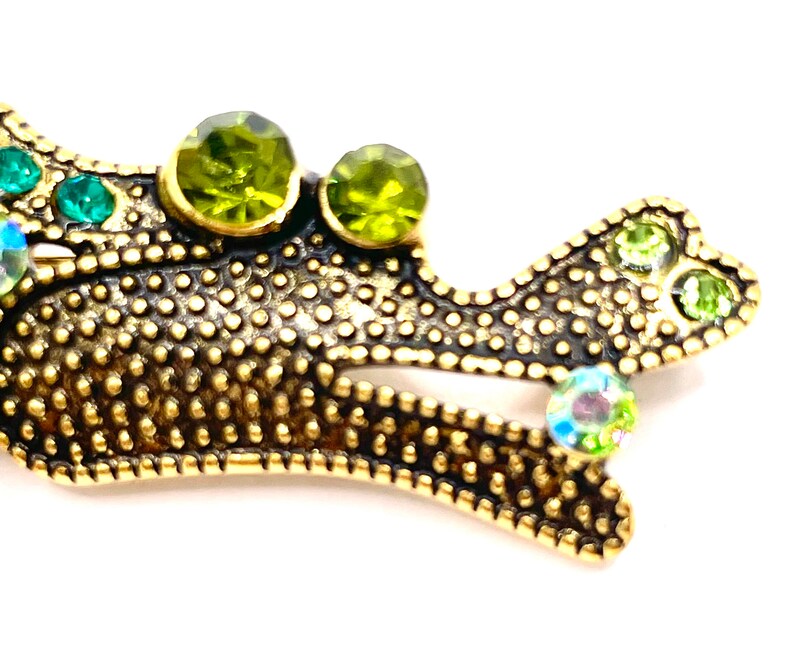 May include: A gold metal brooch in the shape of a stylized bird with green and iridescent rhinestones