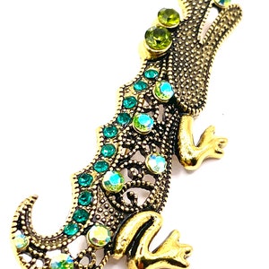 May include: A gold-toned alligator brooch with green and iridescent rhinestones