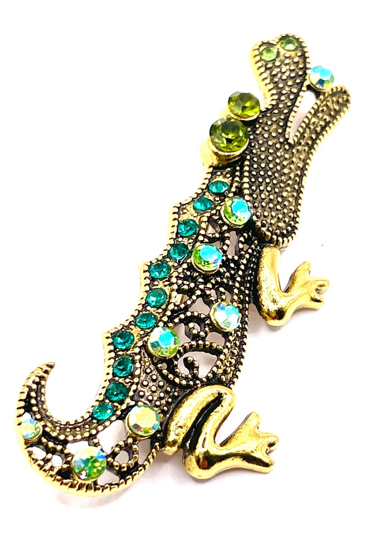 May include: A gold-toned alligator brooch with green and iridescent rhinestones