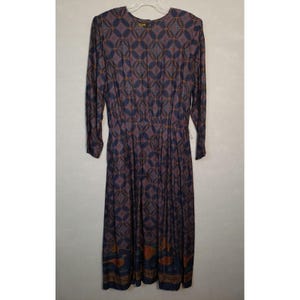 May include: A long-sleeved midi dress in a dark navy blue hue, featuring a repeating geometric circle pattern in muted orange and light blue. The hem displays a border with stylized bird illustrations in orange and brown tones.