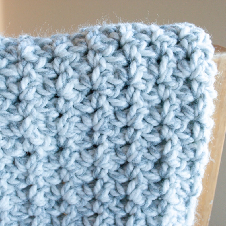 May include: Close-up of a crocheted blanket with a white and gray yarn pattern.