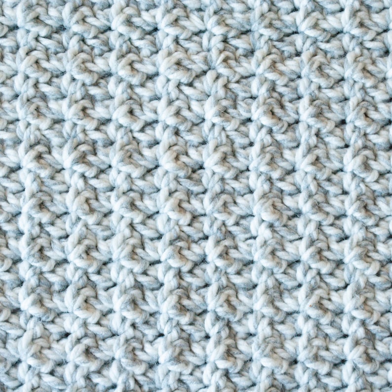 May include: Close-up of a knitted fabric with a textured pattern. The fabric is a mix of white and gray yarn.