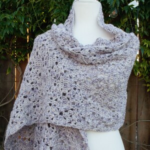 May include: A crocheted shawl in a light purple and white color combination. The shawl is draped over a white mannequin and has a lacy, openwork design.