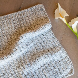 May include: A gray crocheted blanket with a textured pattern. The blanket is folded in half and the edges are visible.