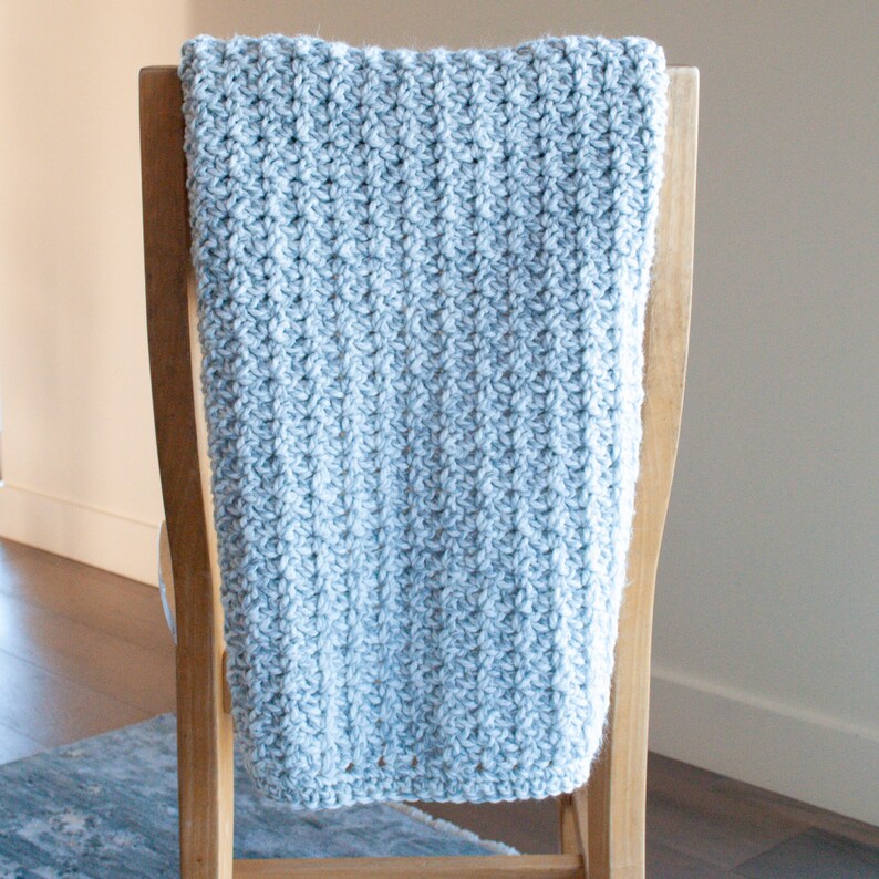 May include: A light blue crocheted throw blanket draped over a wooden chair.