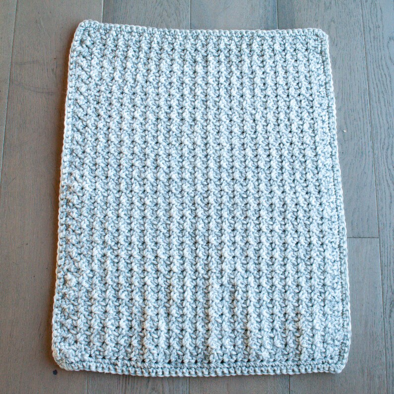 May include: A gray and white crocheted blanket with a textured pattern. The blanket is made with a soft yarn and has a subtle sheen.