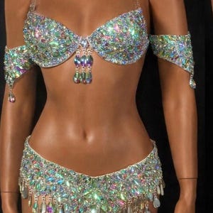 Pode incluir: Um conjunto de duas pe&ccedil;as composto por um suti&atilde; e uma cueca a condizer, ambos ricamente decorados com cristais iridescentes multicoloridos em forma de l&aacute;grima. O suti&atilde; tem al&ccedil;as transparentes e detalhes de cristais pendentes, enquanto a cueca apresenta franjas de cristais.