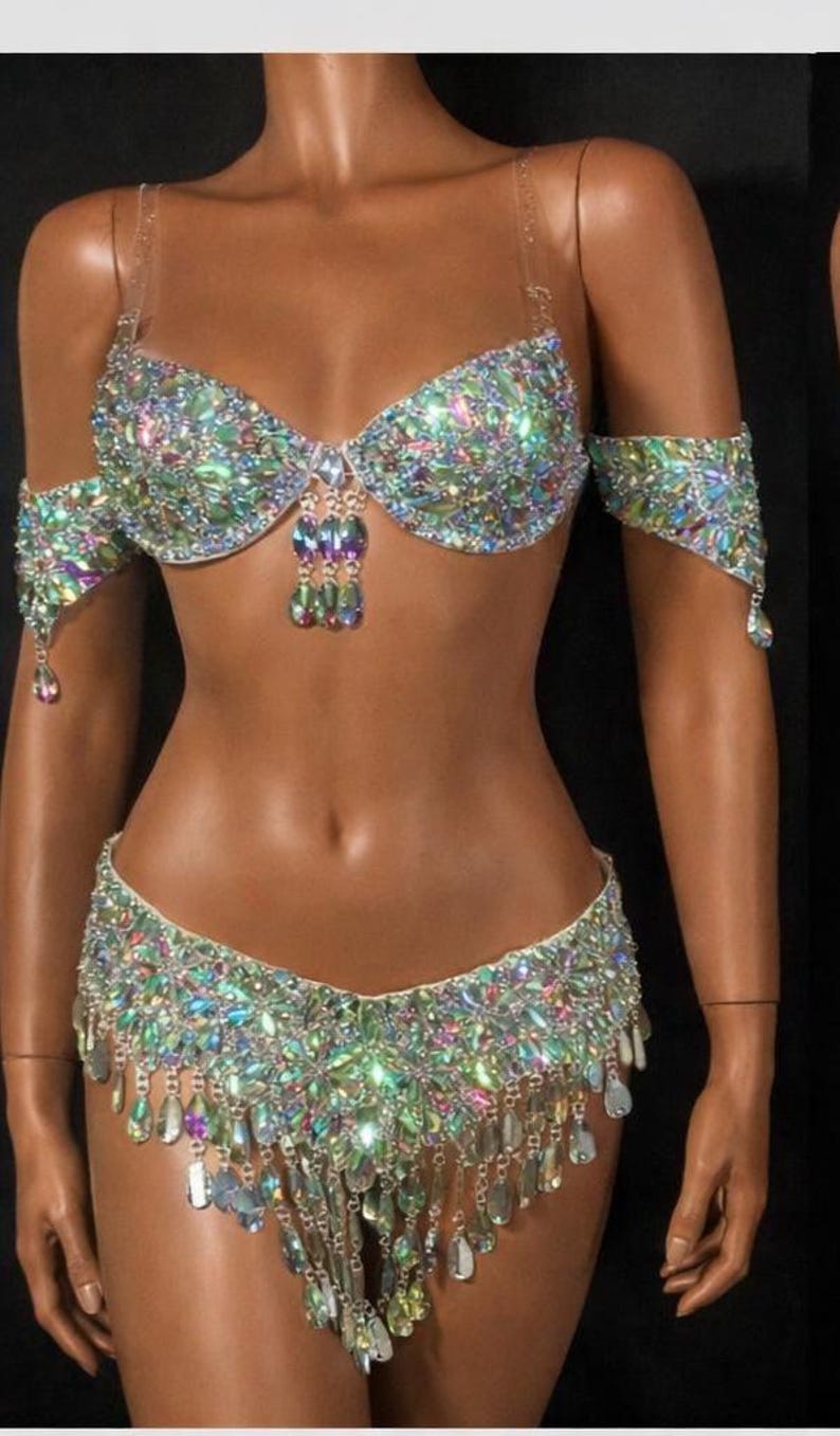 Pode incluir: Um conjunto de duas pe&ccedil;as composto por um suti&atilde; e uma cueca a condizer, ambos ricamente decorados com cristais iridescentes multicoloridos em forma de l&aacute;grima. O suti&atilde; tem al&ccedil;as transparentes e detalhes de cristais pendentes, enquanto a cueca apresenta franjas de cristais.
