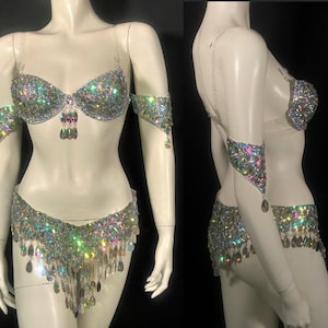 Pode incluir: Um conjunto de duas pe&ccedil;as composto por um suti&atilde; e uma parte de baixo a condizer, ambos ricamente decorados com strass iridescentes multicoloridos e cristais pendentes em forma de gota. O suti&atilde; tem al&ccedil;as transparentes e inclui bra&ccedil;adeiras a condizer.