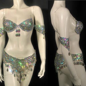 Pode incluir: Um conjunto de duas pe&ccedil;as composto por um suti&atilde; e uma parte de baixo a condizer, ambos ricamente decorados com strass iridescentes multicoloridos e cristais pendentes em forma de gota. O suti&atilde; tem al&ccedil;as transparentes e inclui bra&ccedil;adeiras a condizer.