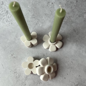 May include: Three white ceramic flower-shaped candle holders with two green candles.