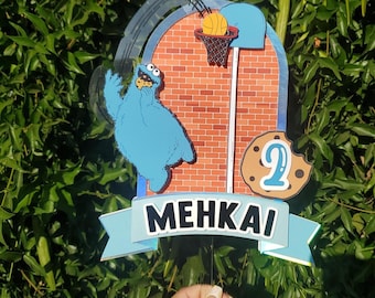 May include: A blue and brown cake topper featuring a cartoon character, basketball hoop, and a cookie with the number 2. The banner at the bottom reads MEHKAI.