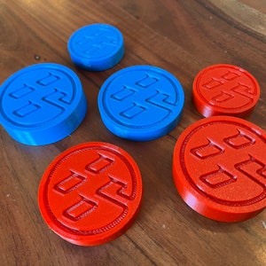May include: Six round, 3D printed game pieces. Three are blue with a white symbol and three are orange with a white symbol.