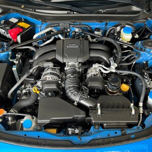 May include: A close-up view of a blue car engine with black hoses and a black air filter. The engine is clean and well-maintained. The engine has a black plastic cover with the text "D4-S" printed on it.