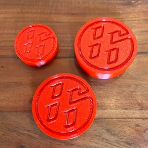 May include: Three red plastic circular coasters with a raised embossed Toyota logo. The coasters are different sizes.