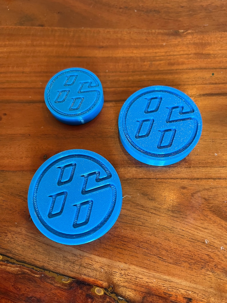 May include: Three blue plastic coasters with a raised, embossed design of the Toyota logo. The coasters are round and have a slightly textured surface.