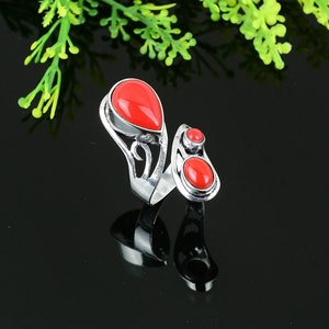 Könnte beinhalten: Ein silberner Ring mit einem roten Stein-Design. Der Ring hat einen großen tropfenförmigen Stein und einen kleineren runden Stein.