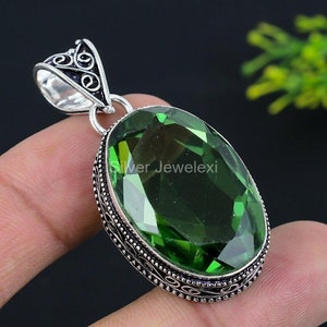 Puede incluir: Un colgante de plata con una piedra preciosa verde de forma ovalada. El colgante tiene un diseño de plata intrincado alrededor de la piedra preciosa.