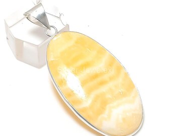 May include: An oval-shaped pendant featuring a polished yellow and white banded gemstone set in a smooth silver-toned metal frame. The pendant includes a triangular silver-toned bail at the top for attachment, showcasing a smooth, glossy surface.
