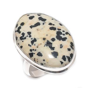 May include: Oval-shaped ring featuring a cream-colored stone with black spots, set in a silver band. The ring has a polished finish and a simple, elegant design. The stone is the focal point, showcasing its unique pattern.
