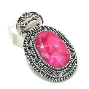 May include: A silver ring featuring an oval, pink gemstone. The gemstone is set within a detailed, ornate silver frame. The ring's band has a decorative design, and the overall style is vintage.