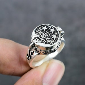 May include: A silver ring with a detailed design of a crescent moon and stars. The ring is openable and has a hinged lid.