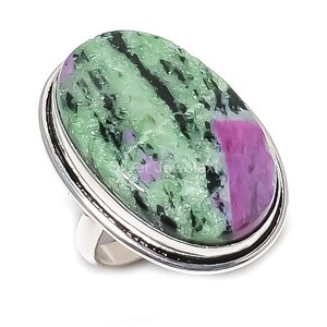 May include: A silver ring with a large, oval gemstone. The stone is a blend of green and pink, with a textured appearance. The ring's band is plain, polished silver.