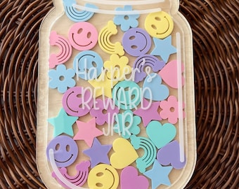 May include: A clear acrylic jar with a wooden lid and a white inscription that reads "Harper's Reward Jar". The jar is filled with colorful plastic shapes, including stars, hearts, rainbows, and smiley faces.