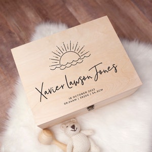 May include: A wooden keepsake box with a sun and waves design. The box is engraved with the name "Xavier Lawson Jones" and the date "18 October 2022, 09:24 AM | 3920G | 54.5CM".