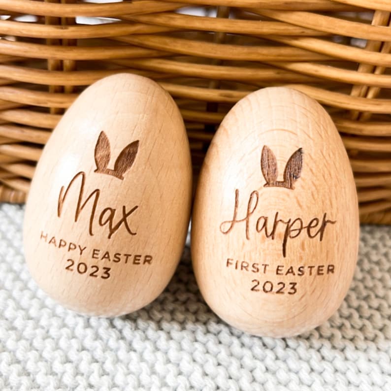 May include: Two wooden Easter eggs with bunny ears engraved on them. One egg says "Max Happy Easter 2023" and the other says "Harper First Easter 2023".